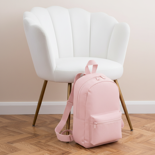 Mini Essential Bagbase Backpack (baby pink) next to white velvet chair