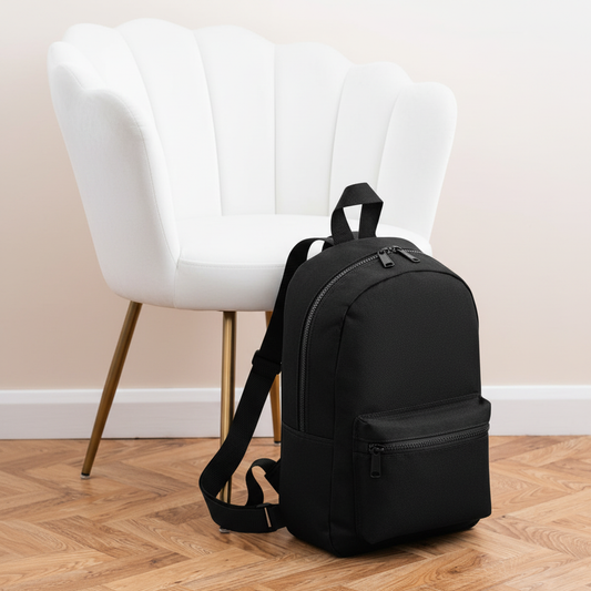 Mini Essential Bagbase Backpack (black) next to white velvet chair