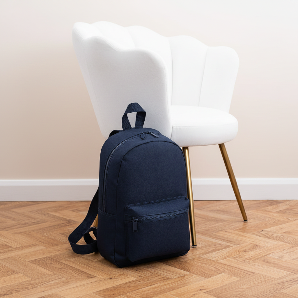 Mini Essential Bagbase Backpack (French navy) next to white velvet chair